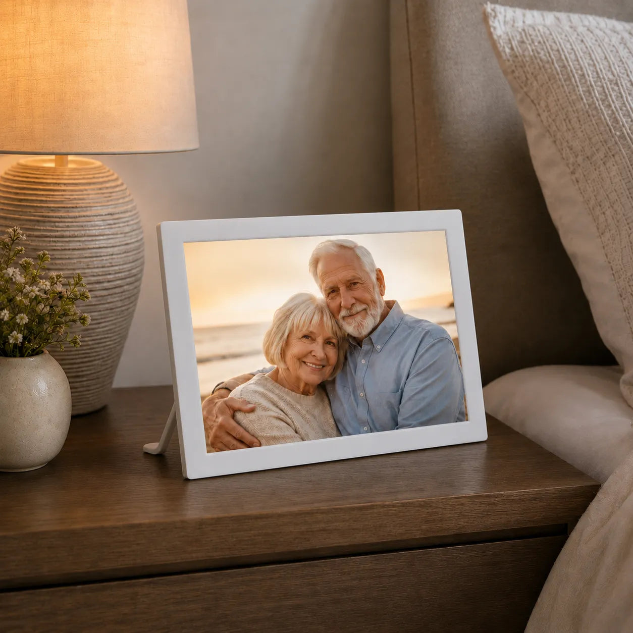 White Pintura cordless digital photo frame on a wooden bedside table displaying a family portrait beside a lamp